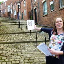 Juliette holds up an image of Lowry's 'Crowther Street' at the setting of the painting
